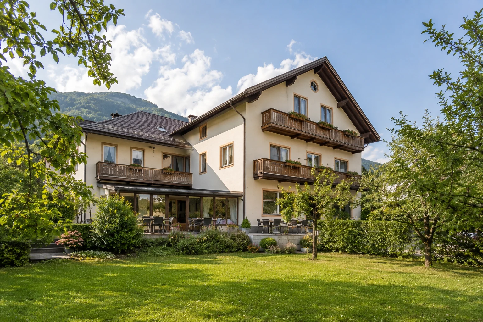 Kleine österreichische Pension mit Holzbalkonen, Gartenterrasse und grüner Umgebung